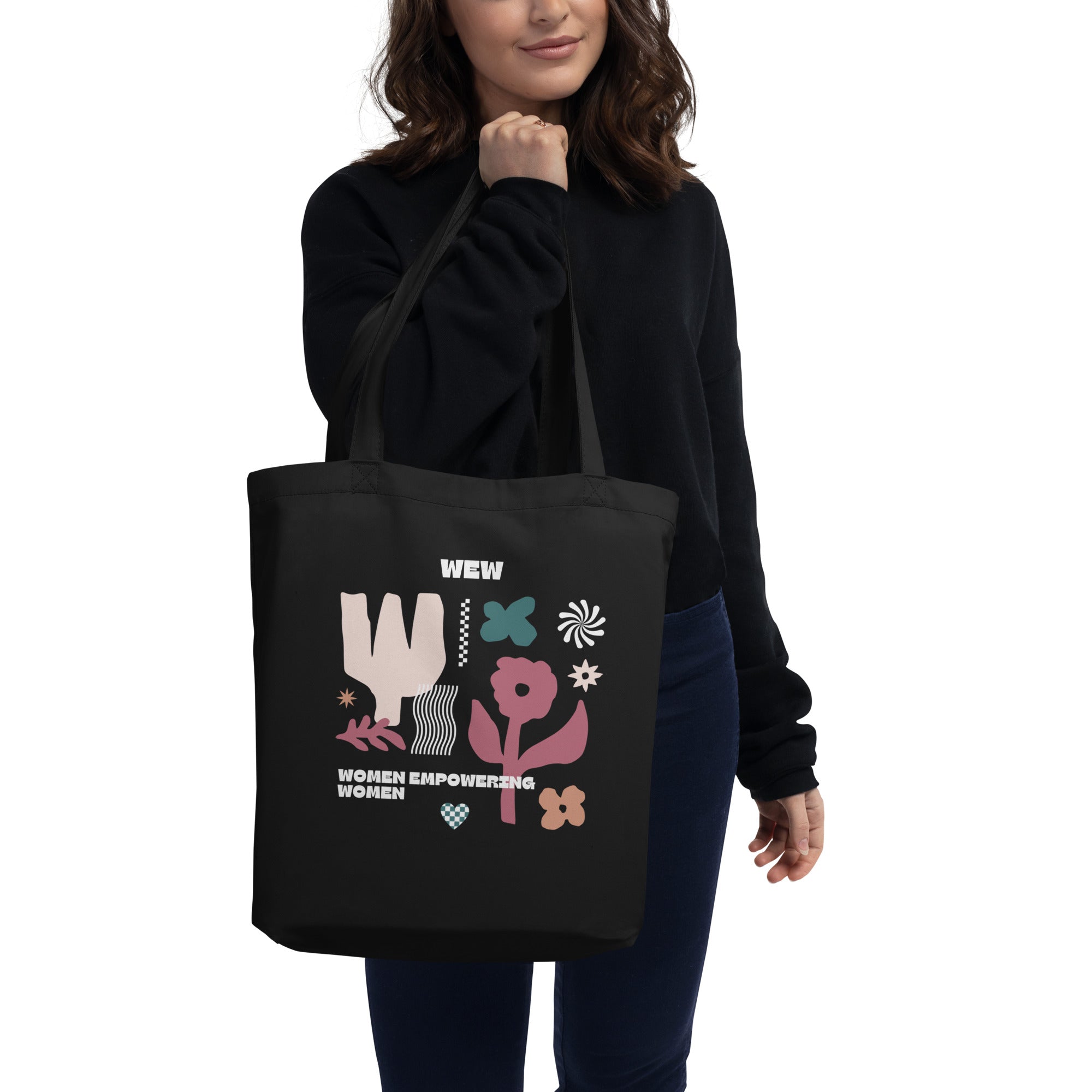 Women posing while holding the black organic tote bag on which there are pink and green flowers along with the phrase women empowering women 