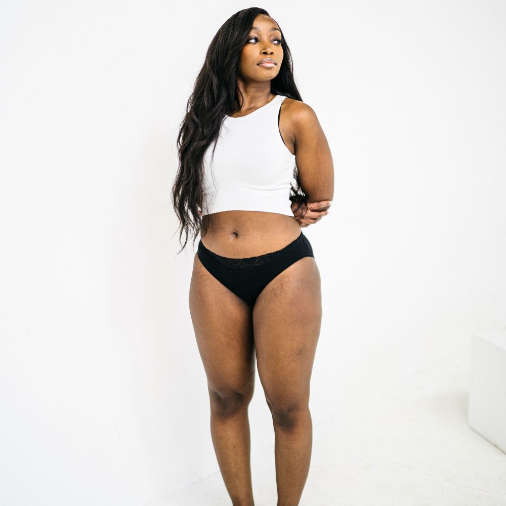 black woman standing wearing white top and black period panties
